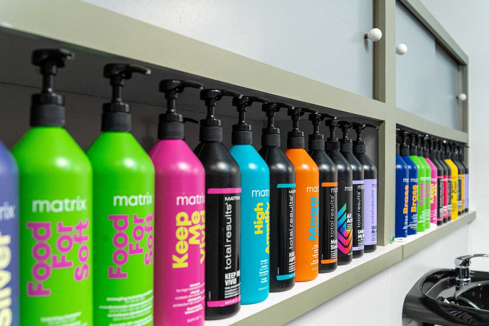 Colorful hair products bottles lined up on wall shelf in a salon.