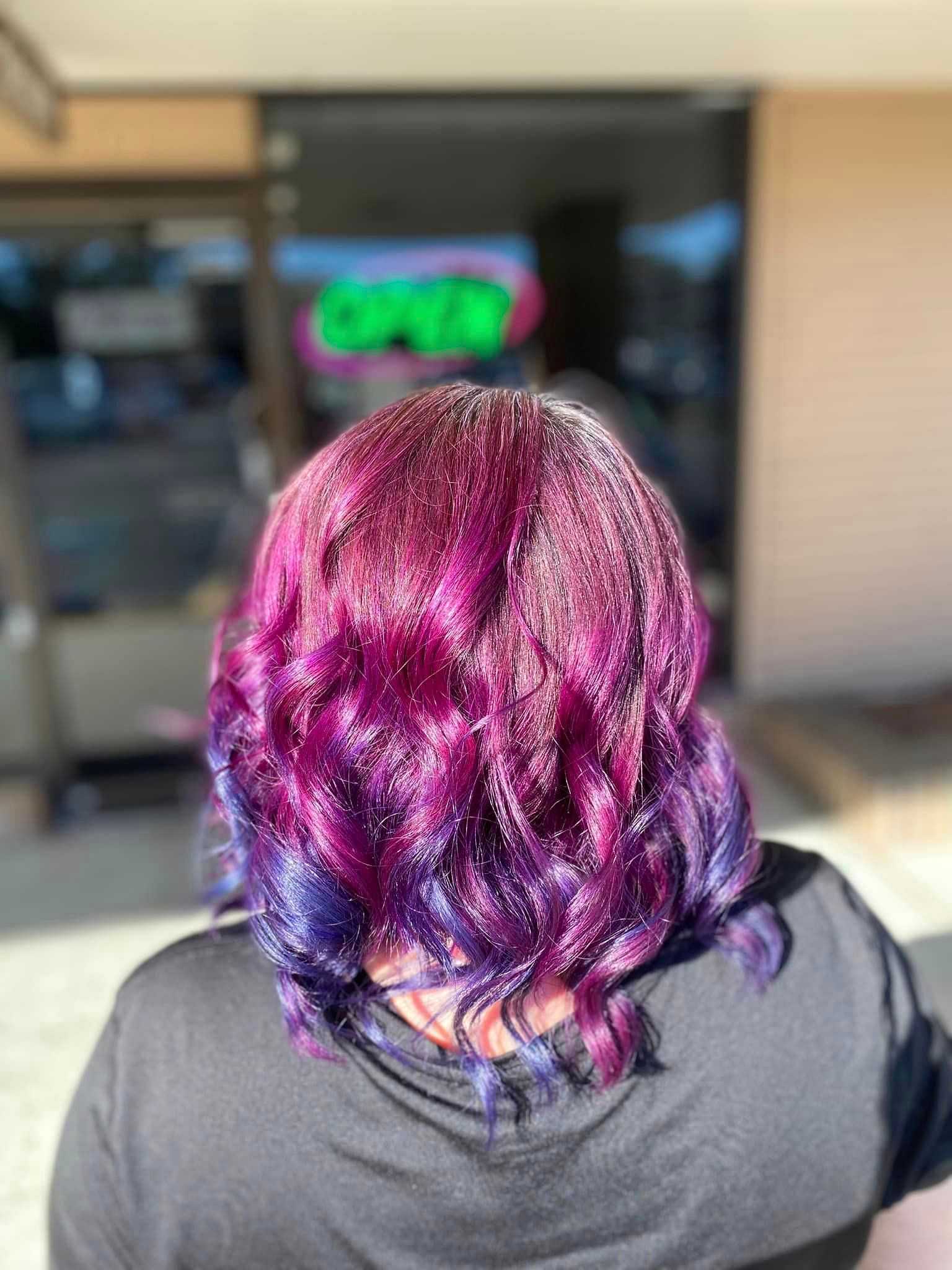 Back view of person with curly, vibrant magenta and purple hair standing outdoors.