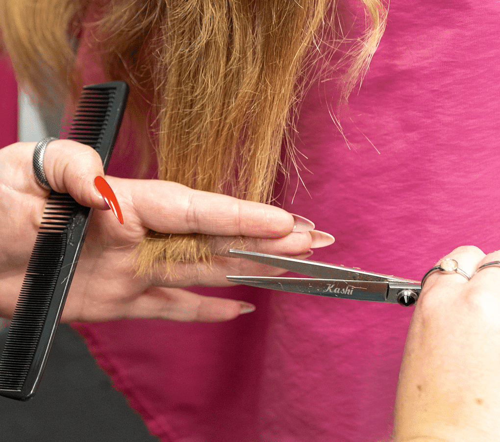 Close-up of a hairdresser cutting a client's hair with scissors, holding a comb for precision.