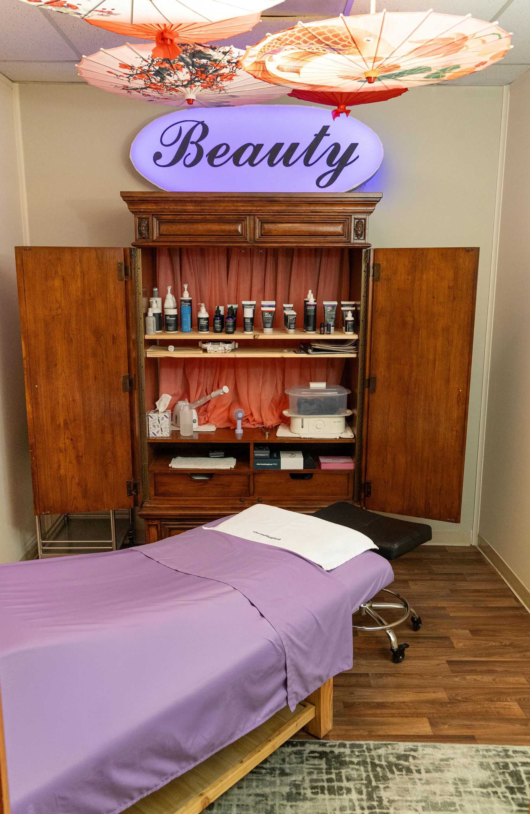 Beauty spa room with a wooden cabinet, skincare products, and a treatment bed with a purple sheet.